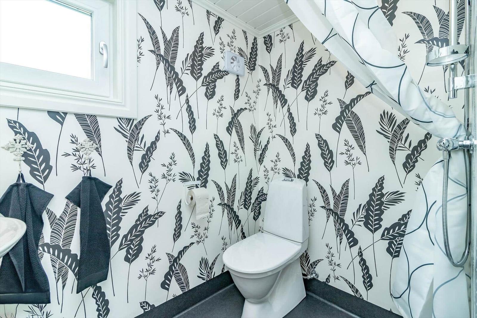 Badezimmer mit Toilette, Dusche und floraler Tapete