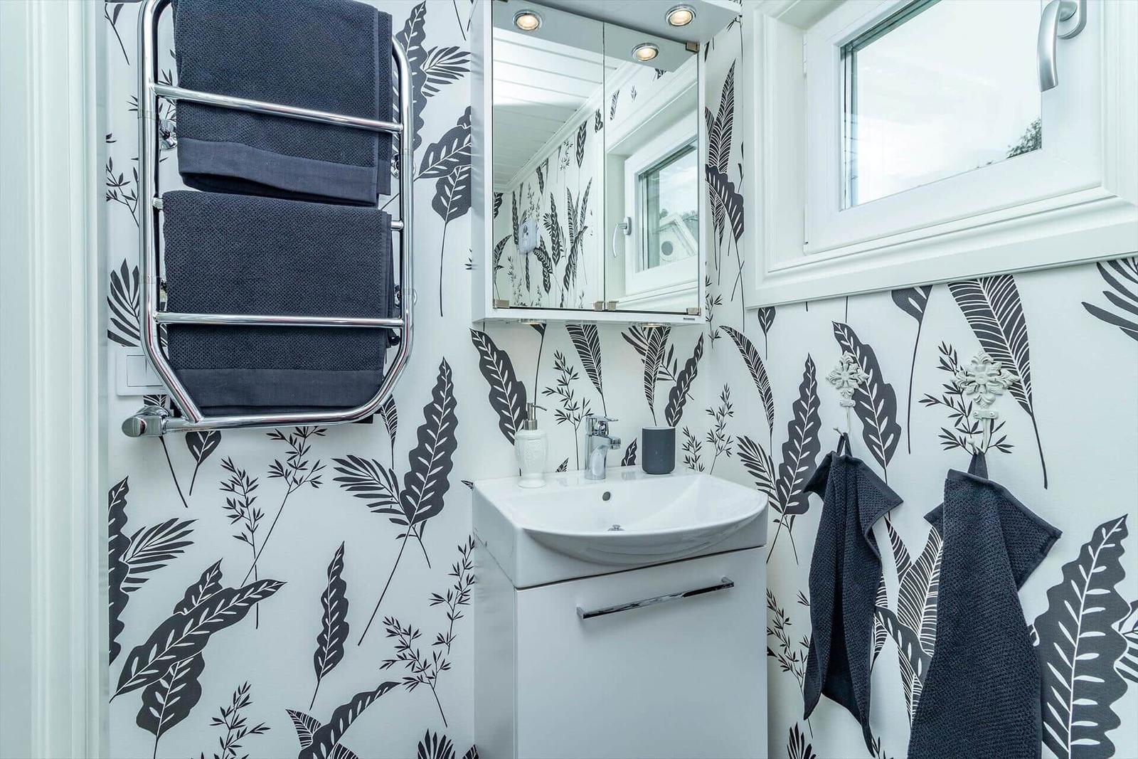 Badezimmer mit Waschbecken, Spiegelschrank und Handtuchhalter an floral gemusterten Wänden.