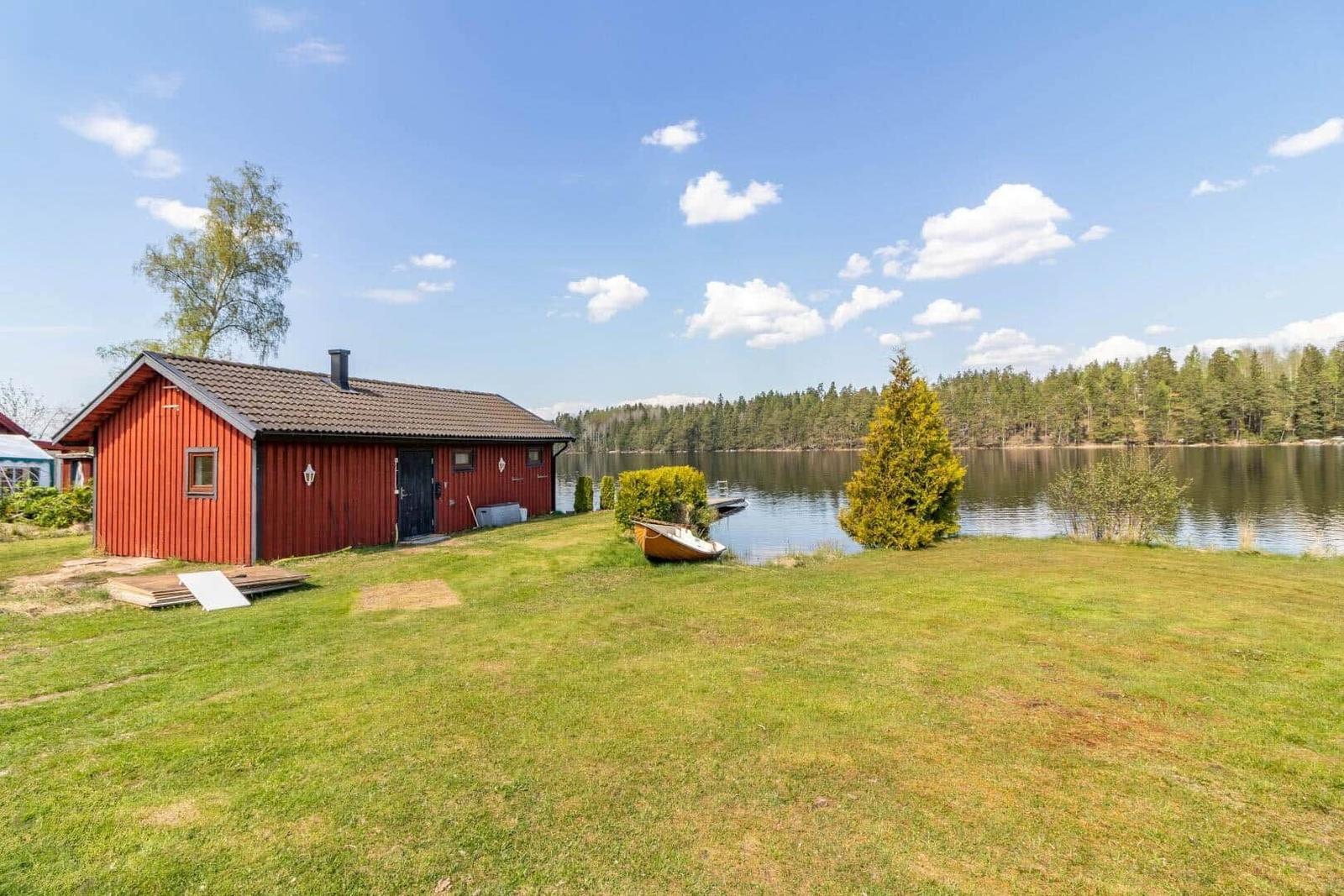 Rotes Holzhaus am See mit Boot und Grasfläche.