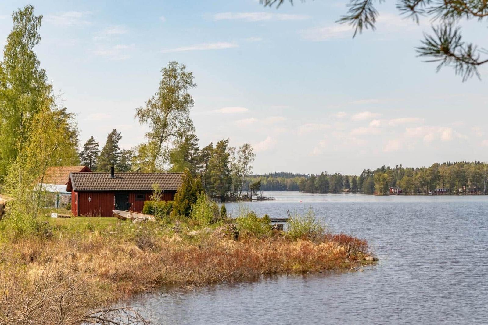 Rotes Holzhaus am Seeufer mit Blick auf Wald und Wasser.