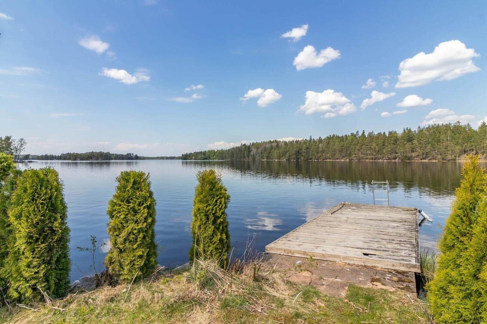 Holzsteg führt zu ruhigem See mit Wald im Hintergrund.