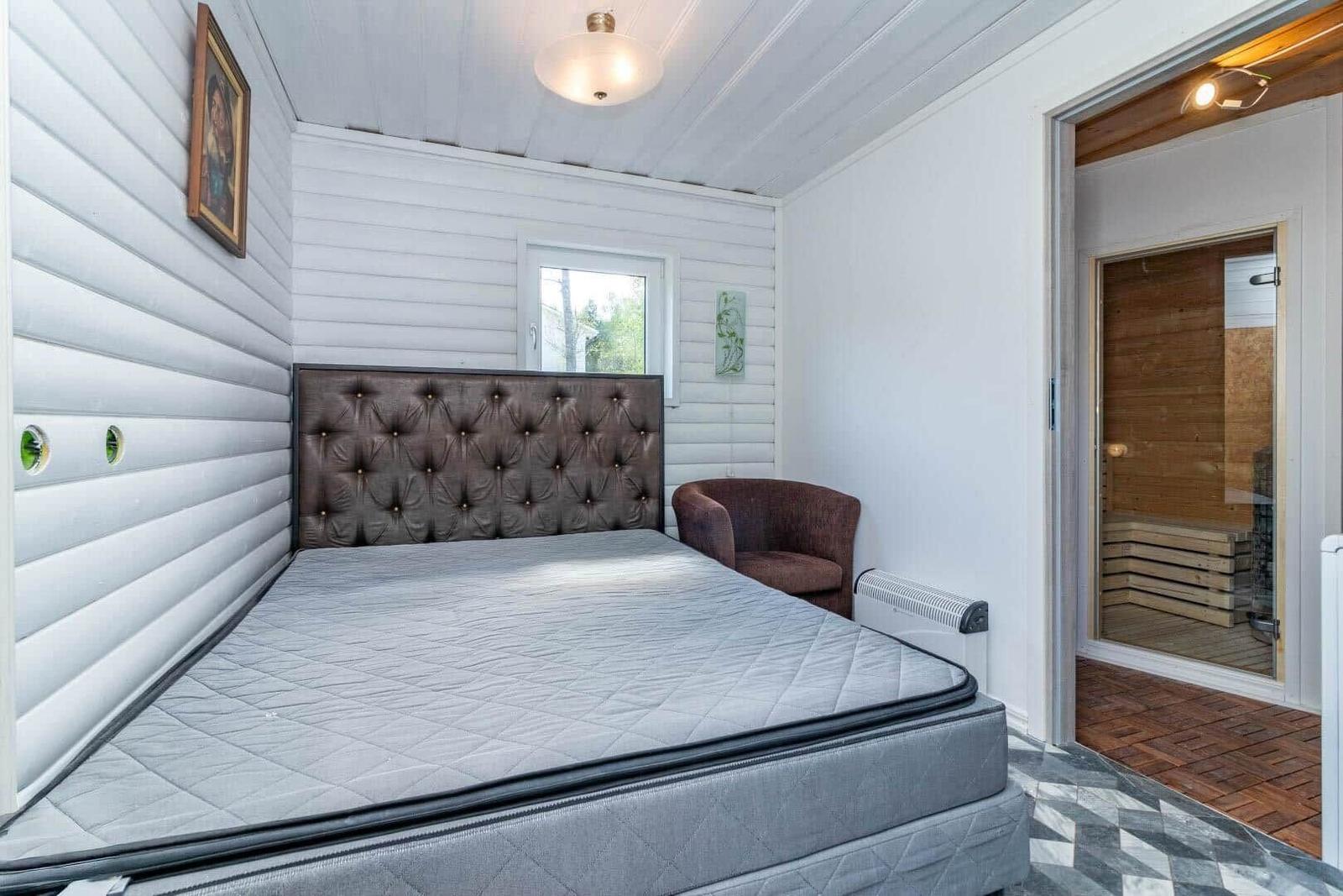Schlafzimmer mit Bett, Sessel und Sauna im Hintergrund.