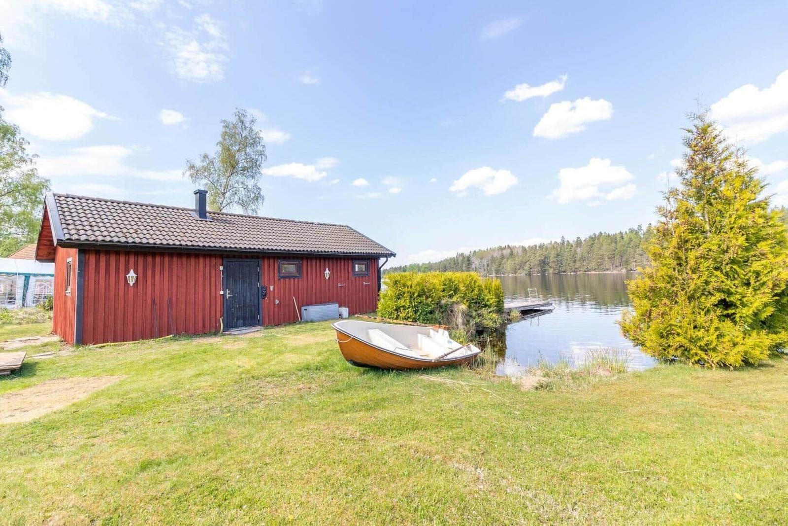 Rotes Holzhaus am See mit Boot und Grillplatz.