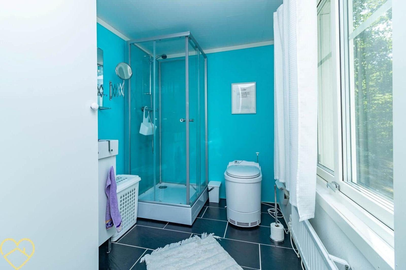 Badezimmer mit Dusche, Toilette und Waschmaschine. Blaue Wände und schwarze Fliesen.
