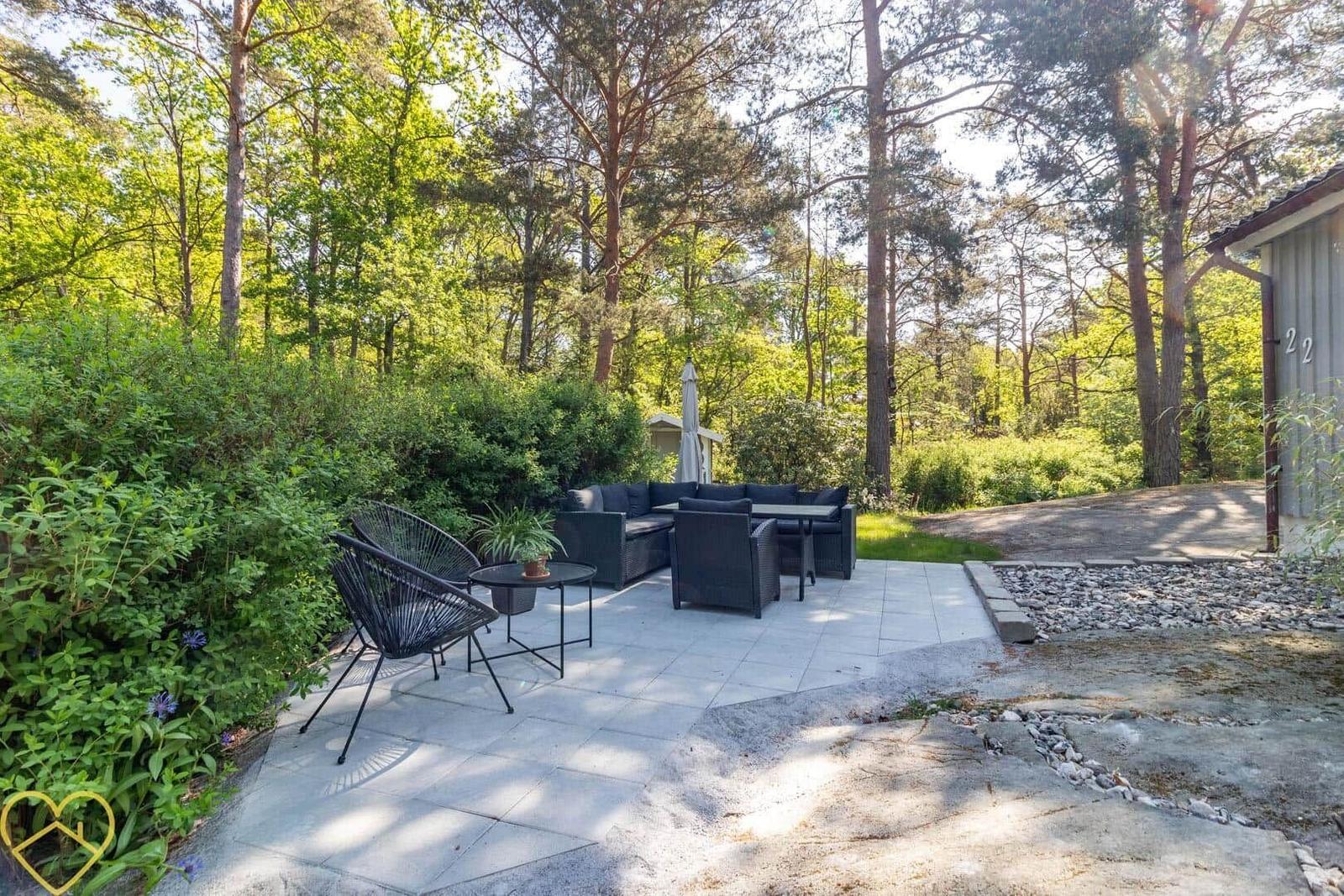Terrasse mit Sitzgruppe und Sonnenschirm im Wald. Pflanzen und Steine umgeben den Platz.