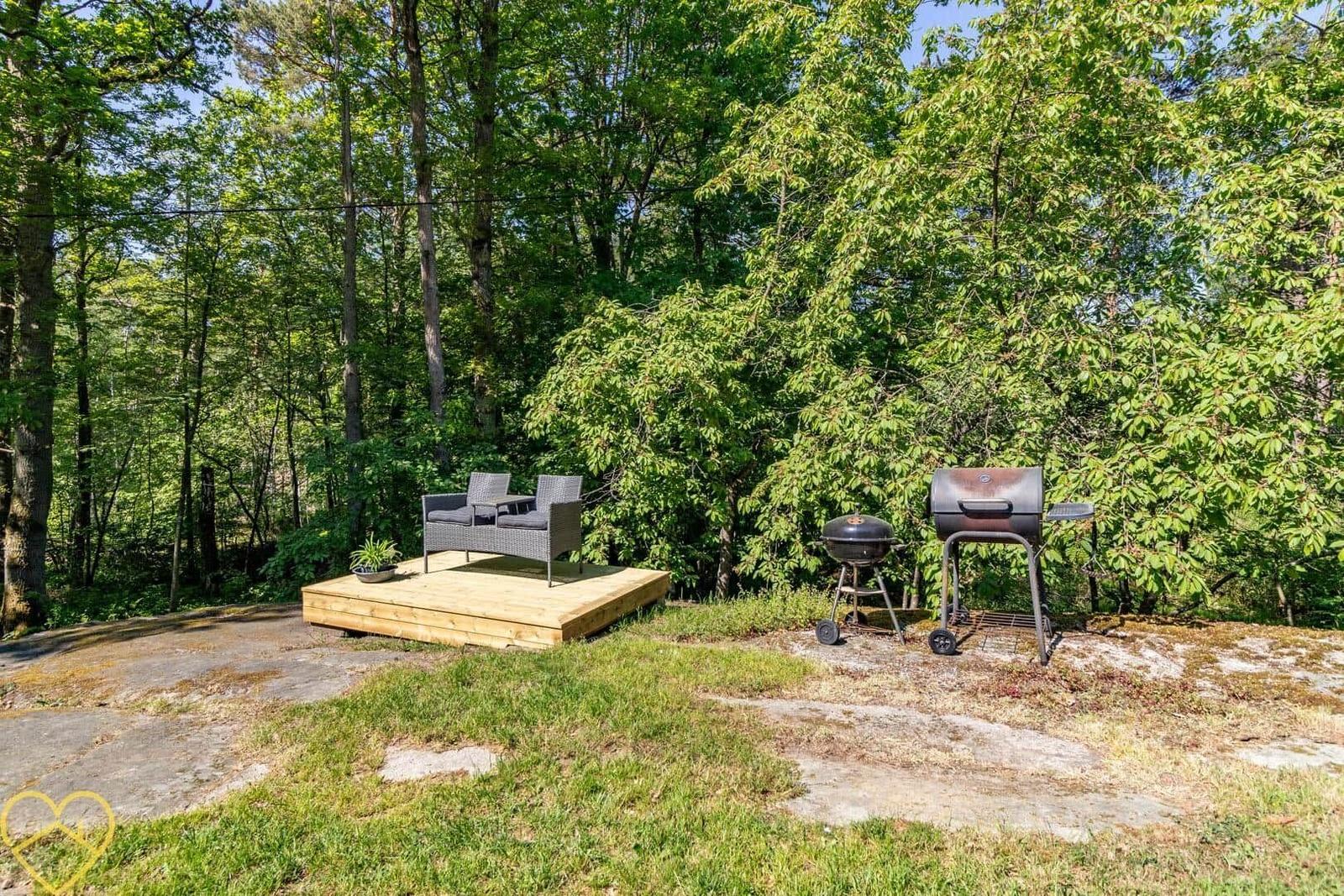 Holzterrasse mit Sitzgruppe und Grill im Wald.