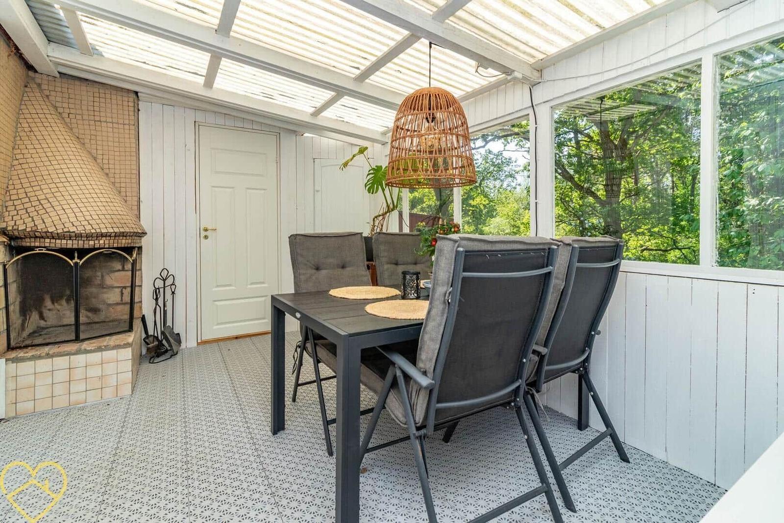 Terrasse mit Esstisch, Stühlen und Kamin. Durchgehendes Glas bietet Blick auf Grün.