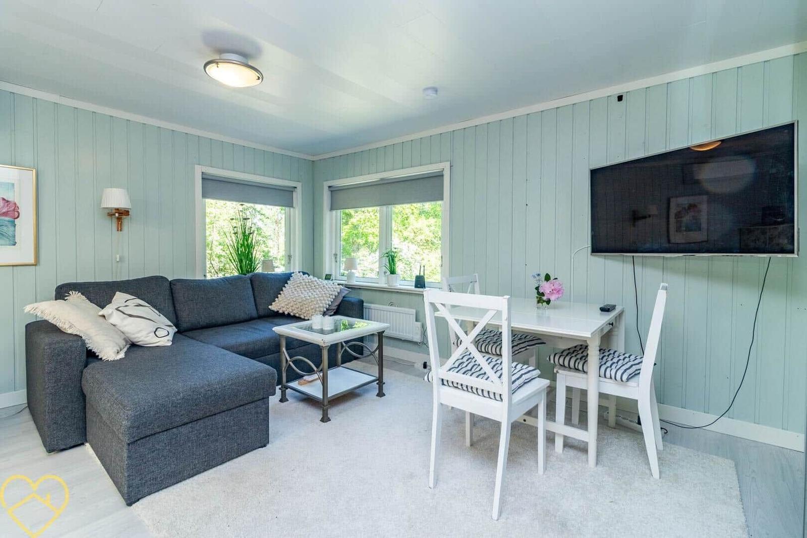 Wohnzimmer mit Sofa, Esstisch und Fernseher an der Wand.
