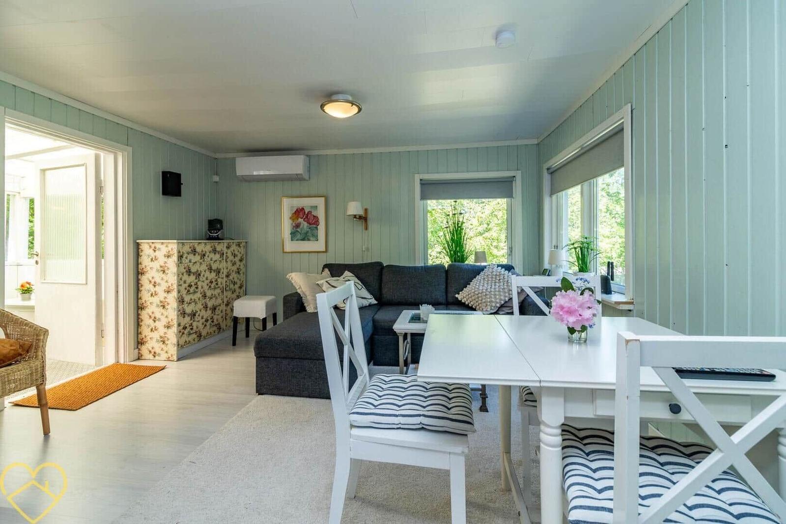 Wohn- und Essbereich mit Sofa, Tisch und Stühlen. Hellblauer Holzwandverkleidung.