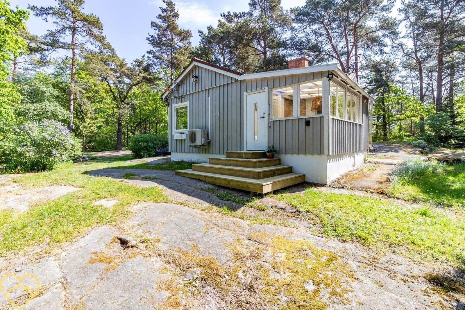 Holzhaus mit Terrasse im Wald. Eingangstreppe und Fenster sichtbar.