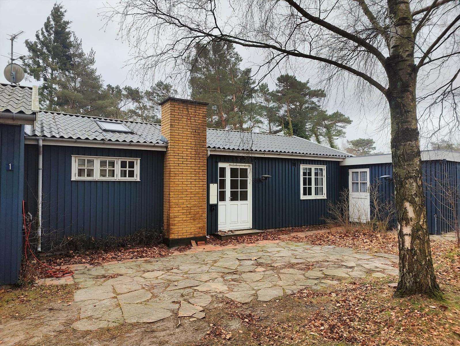 A blue wooden house with white door and windows. Stone path and tree in front of the house.