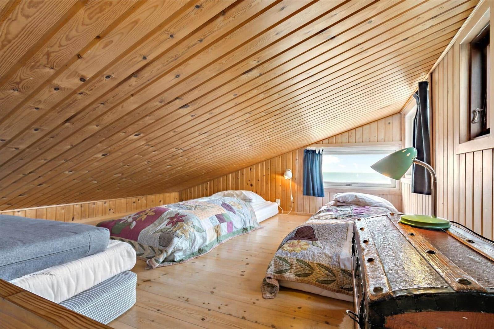 Bedroom with two beds, wood walls, and sloped ceiling. Window with sea view.