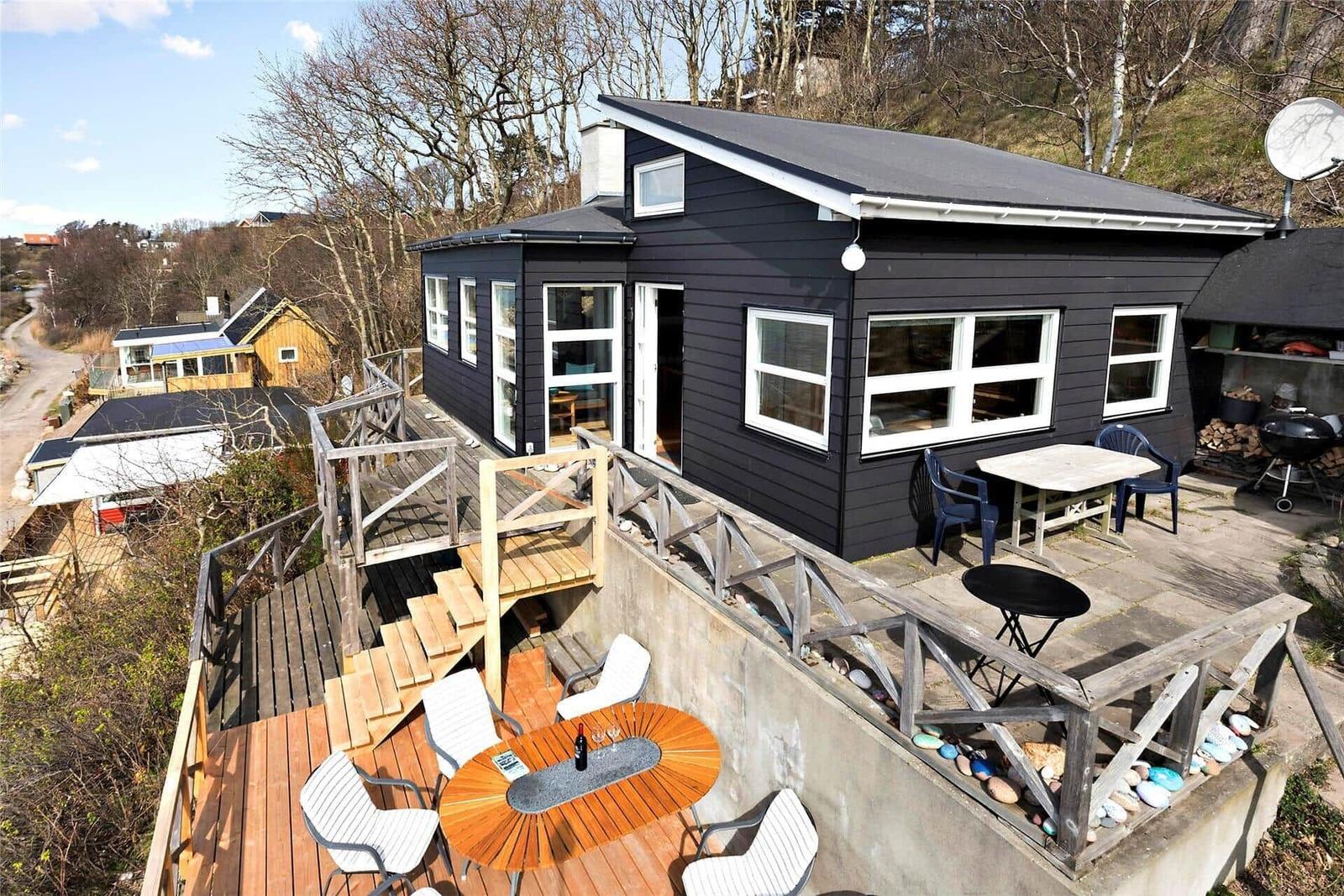 Black house with terrace, tables, and chairs. Wooden terrace with view of surroundings.