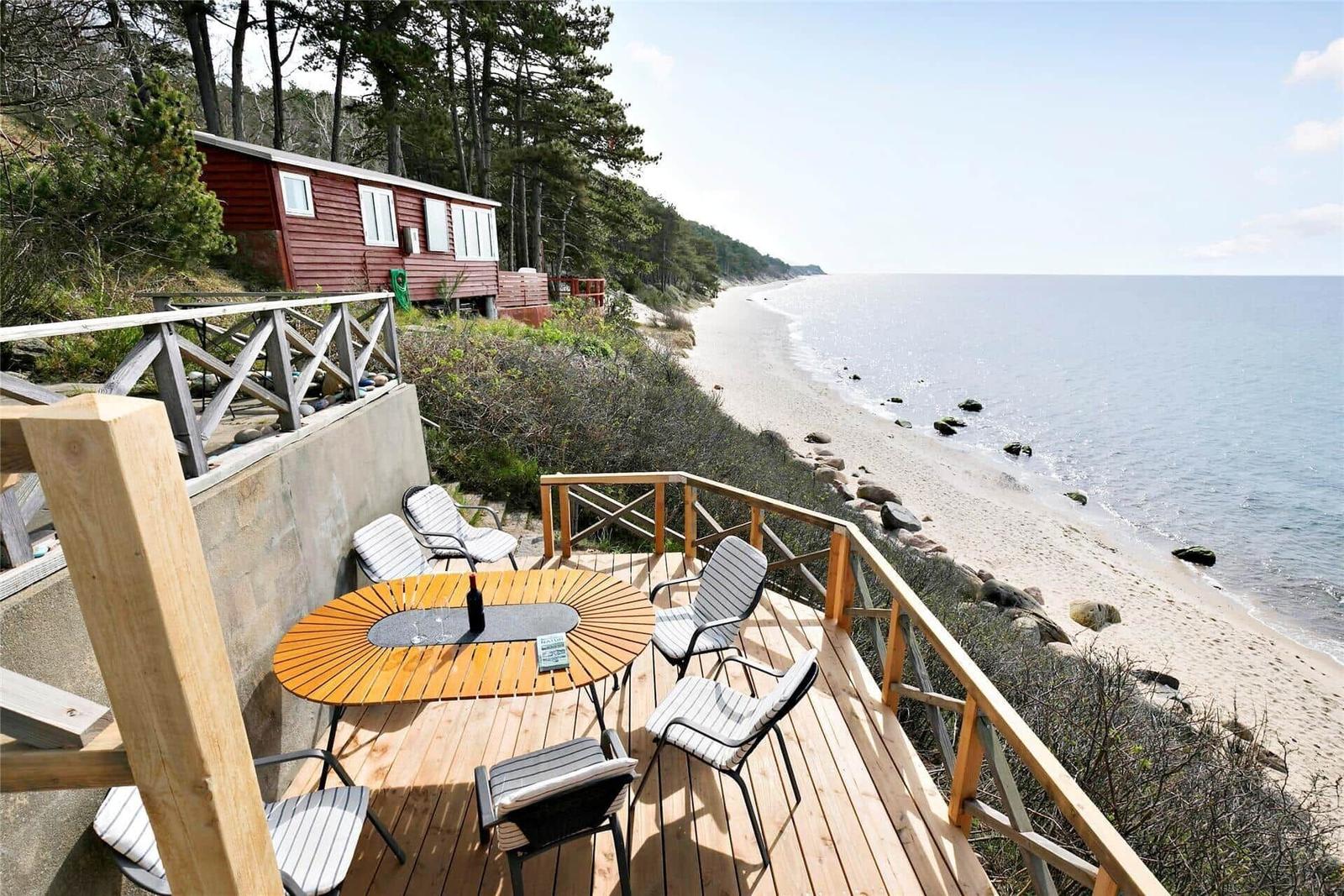 Deck with table and chairs overlooks beach and sea.