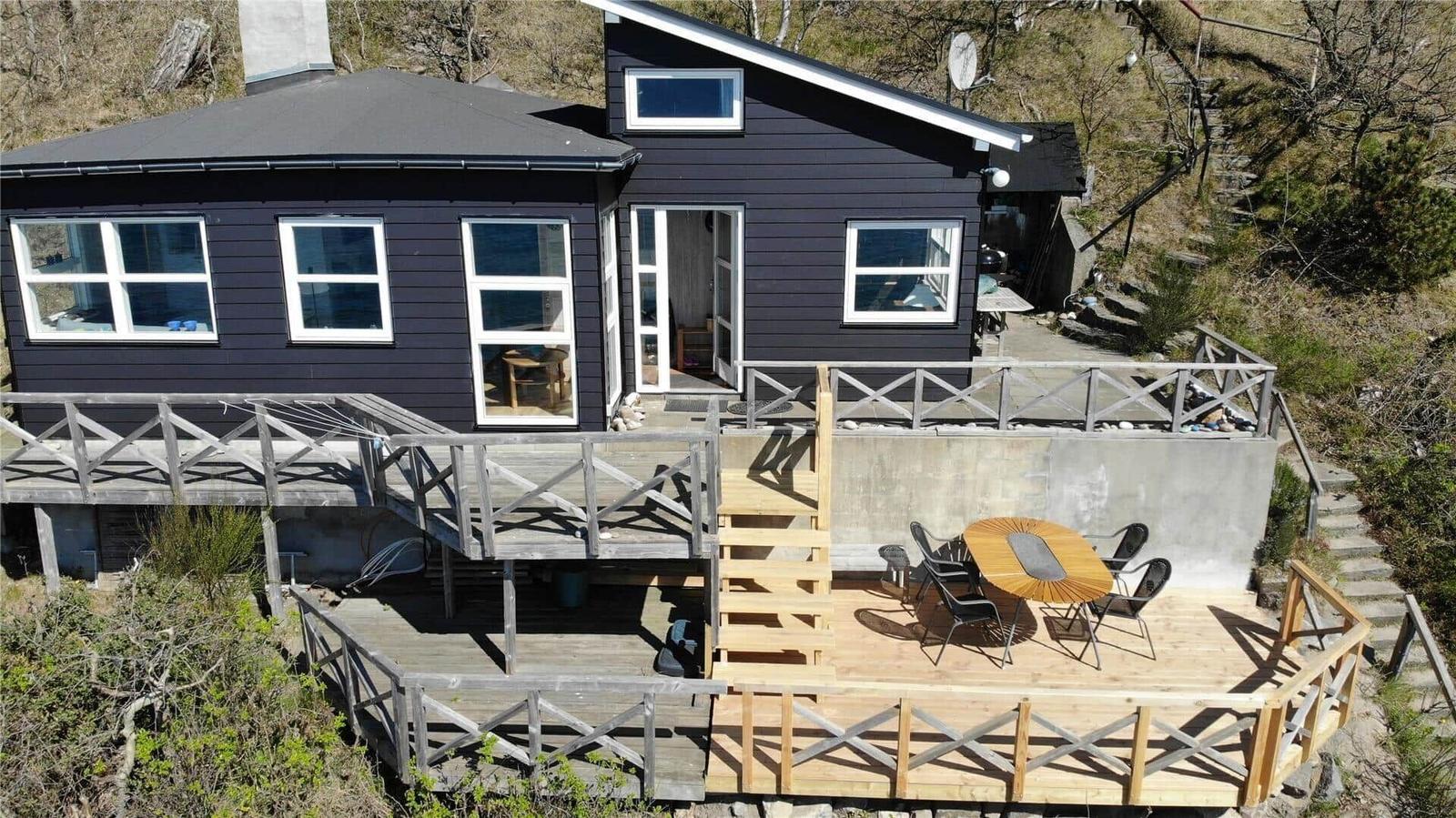 Black house with wooden terrace and outdoor seating area.