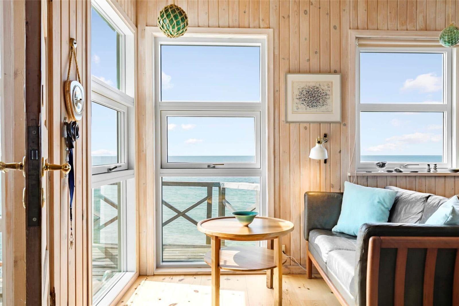 Living room with wooden walls, sofa, and ocean view through large windows.