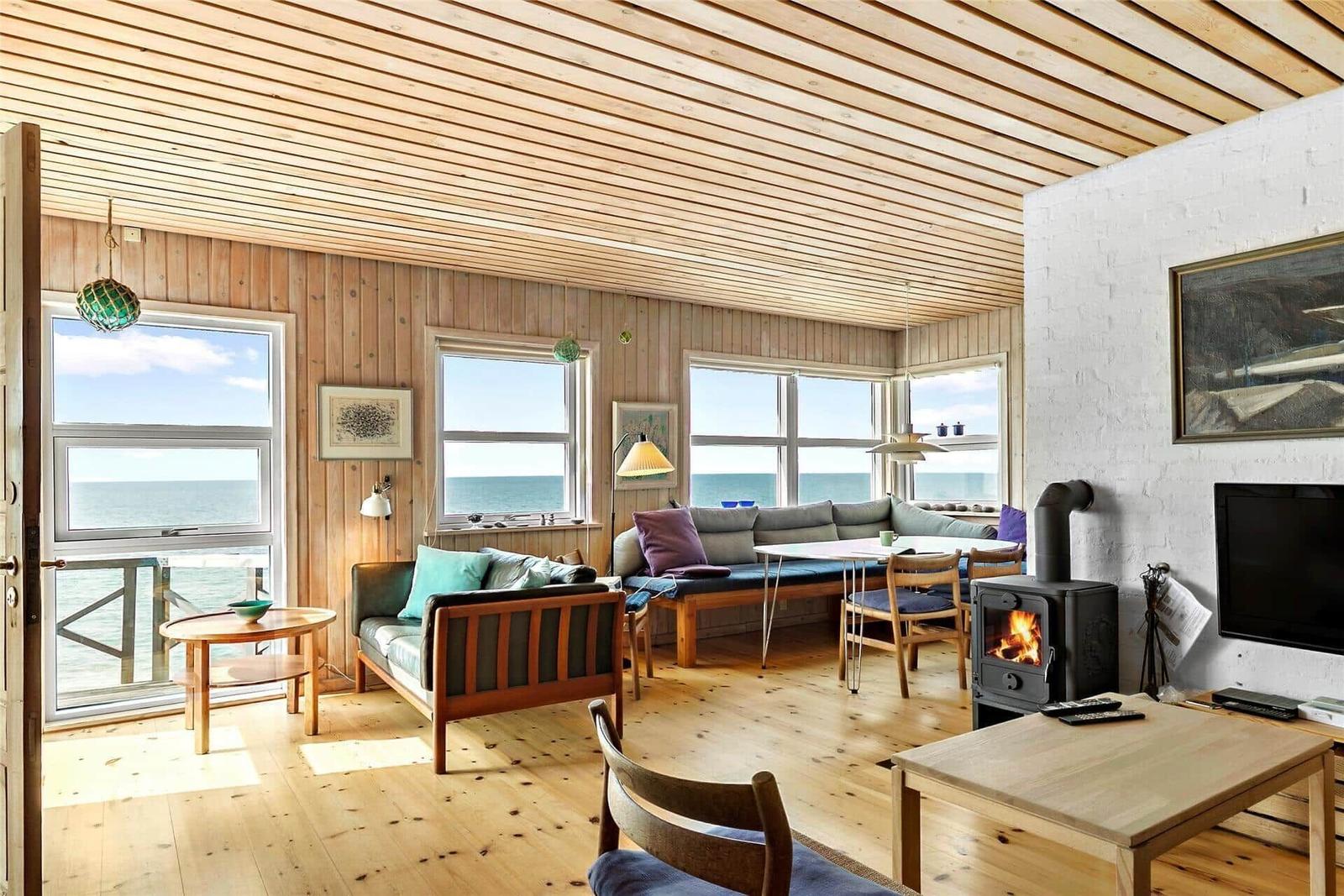 Living room with wooden ceiling, sea view through windows, and wood stove.
