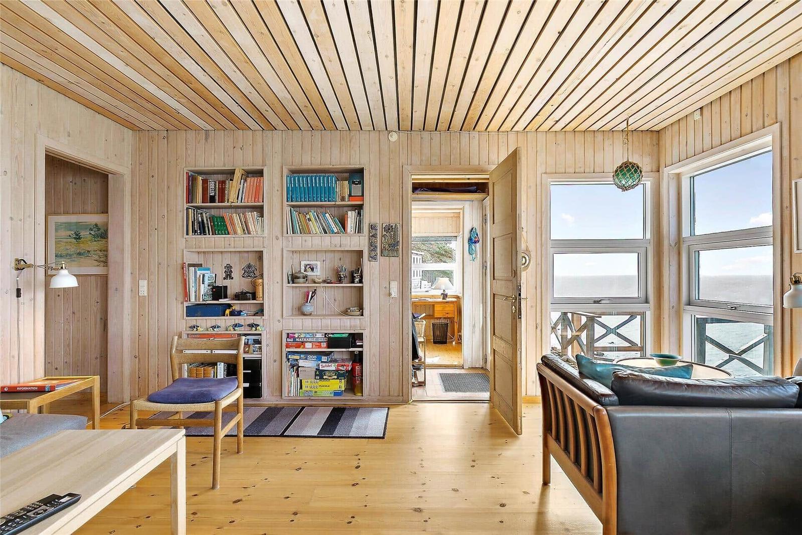 Living room with wood walls, bookshelves, and ocean view through large windows.