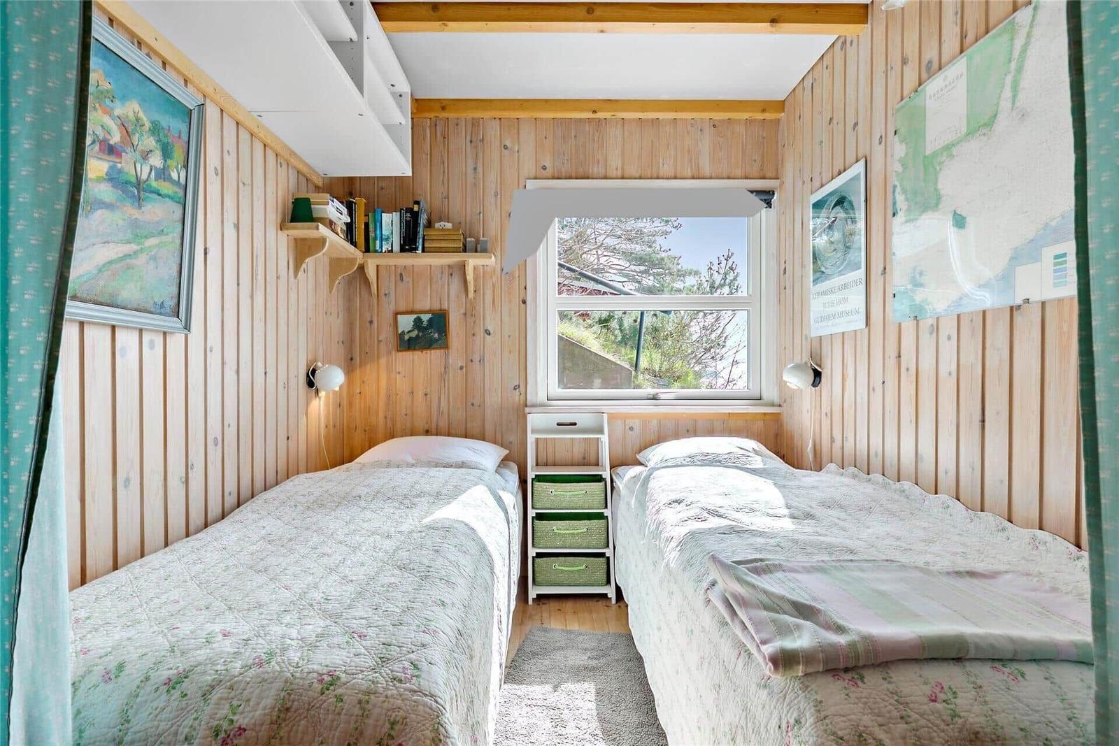 Two beds with patterned bedding, wooden walls, window, and wall shelves.