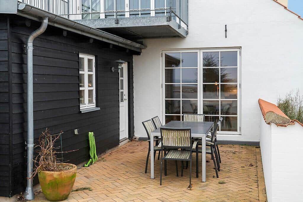 Terrace with table and chairs, black and white house walls, window and plant