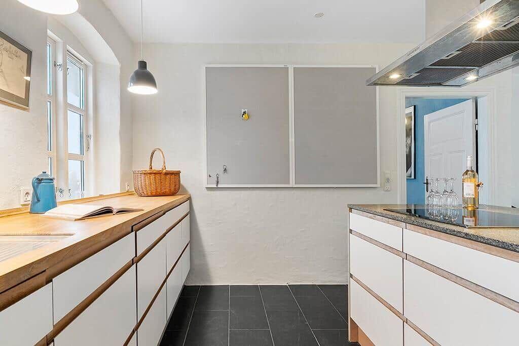 Kitchen with wooden countertop, white cabinets, and window. A board hangs on the wall.