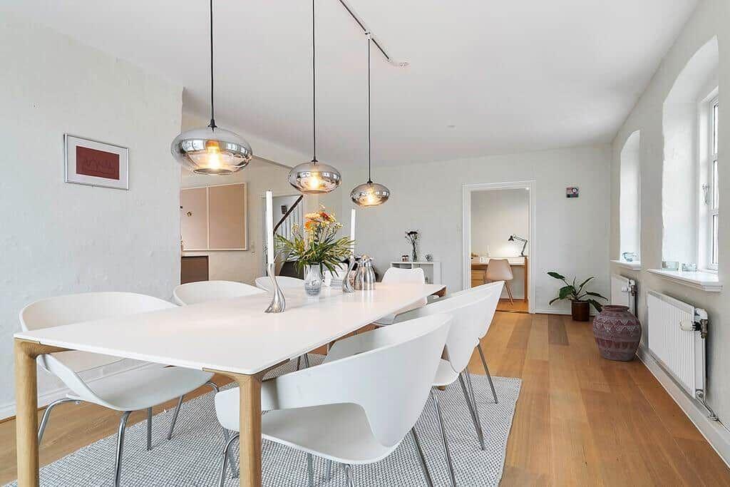 Dining area with white table and chairs, three pendant lights, and hardwood floor.