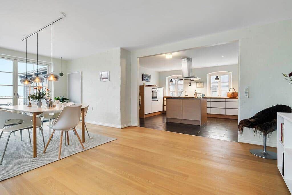Dining area with table and chairs, kitchen with island and windows.