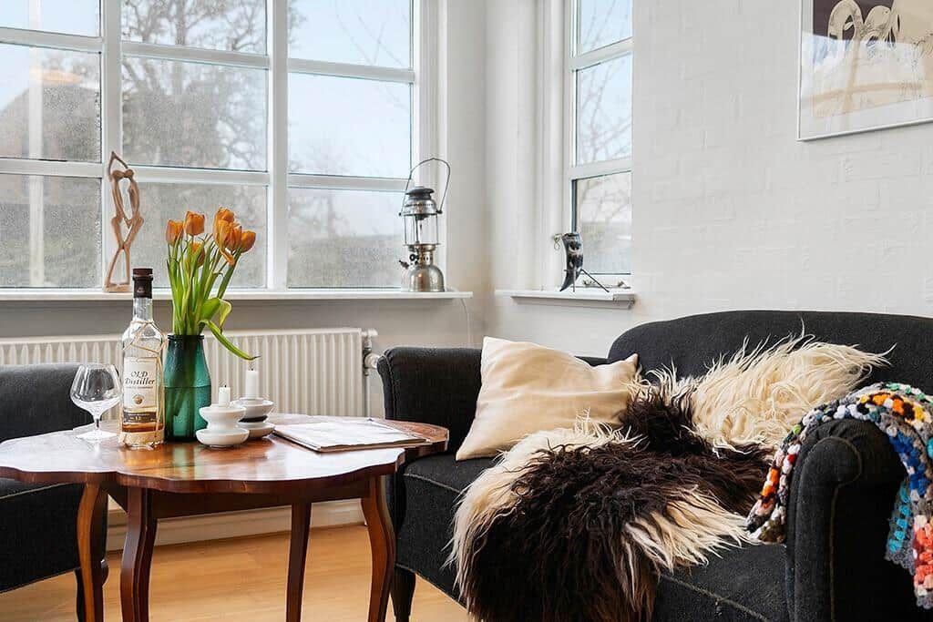 A living room with a dark sofa, wooden table, and windows.