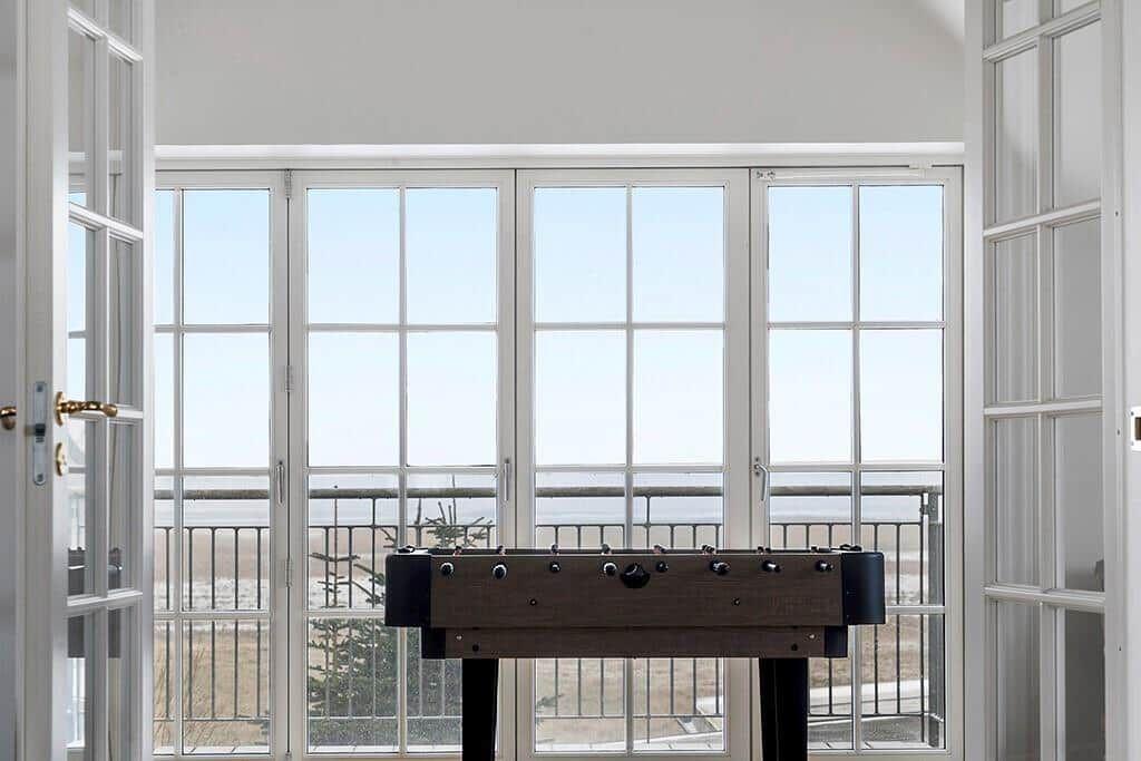 Foosball table in front of large windows with balcony and landscape view.