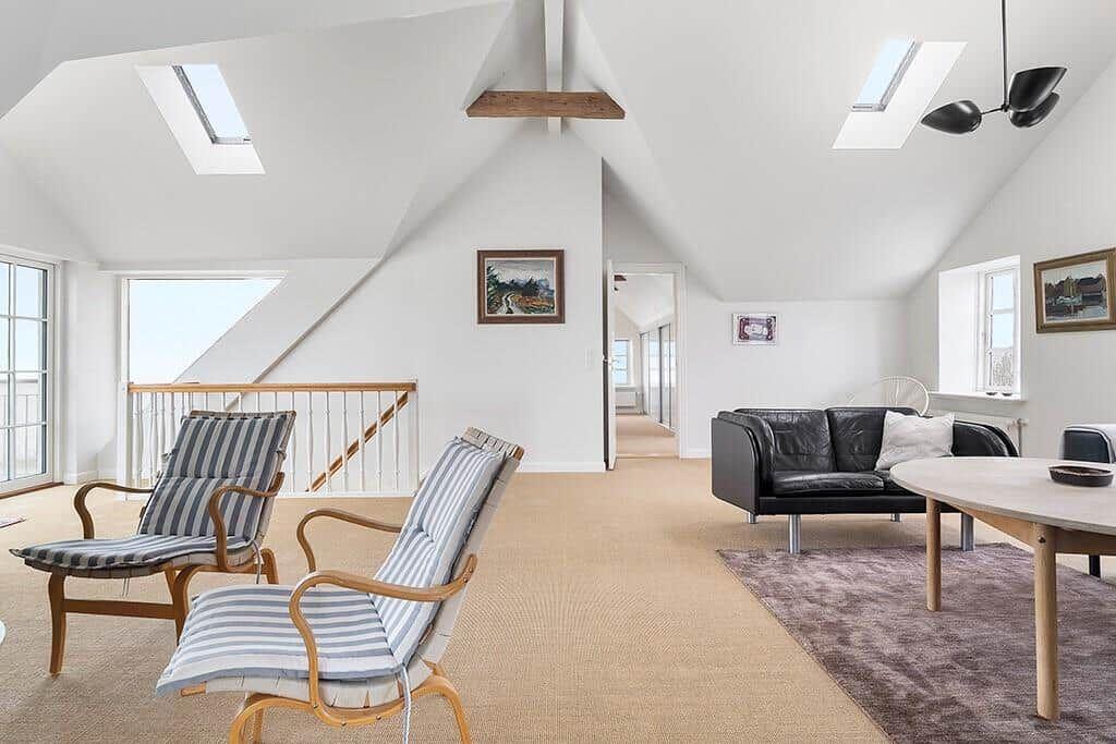 Living space with two chairs, sofa and table under sloped ceilings with skylights.