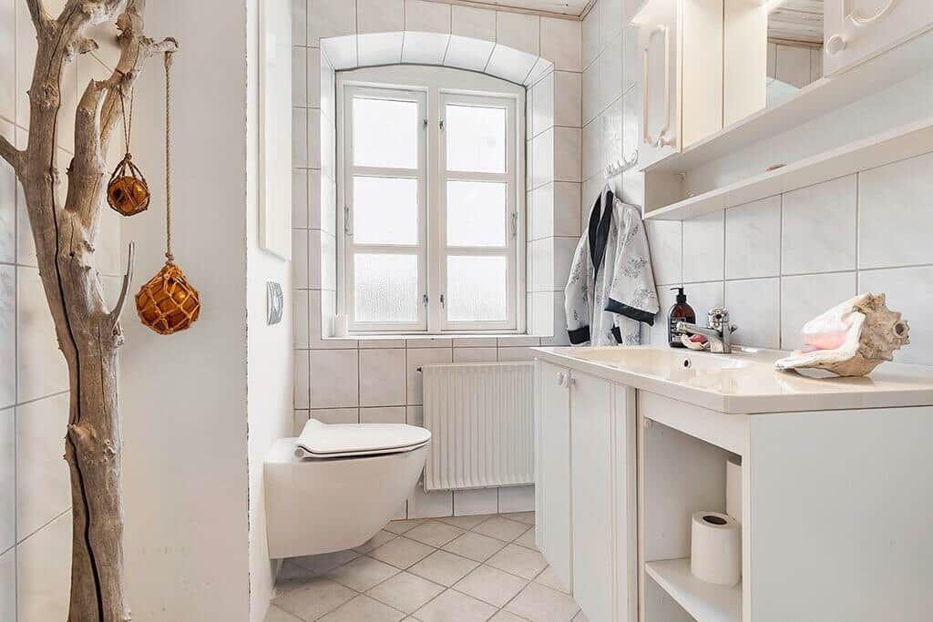 Bathroom with toilet, sink, and window. Wooden decor and seashells are visible.