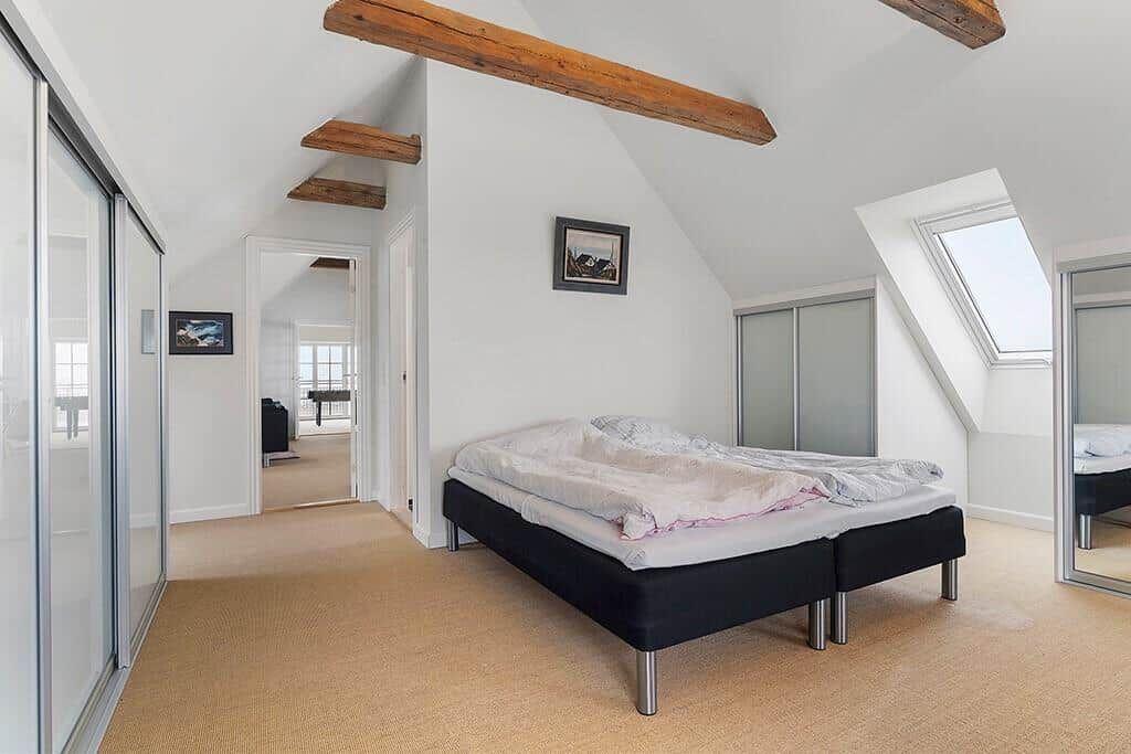 Bedroom with sloped ceiling, wooden beams, and skylight. Black bed, sliding doors, and carpeted floor.