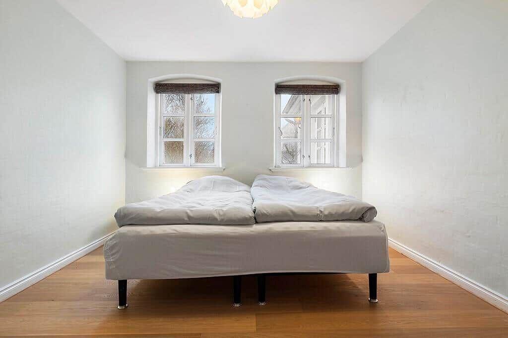 A bedroom with a double bed, two windows, and hardwood floors.