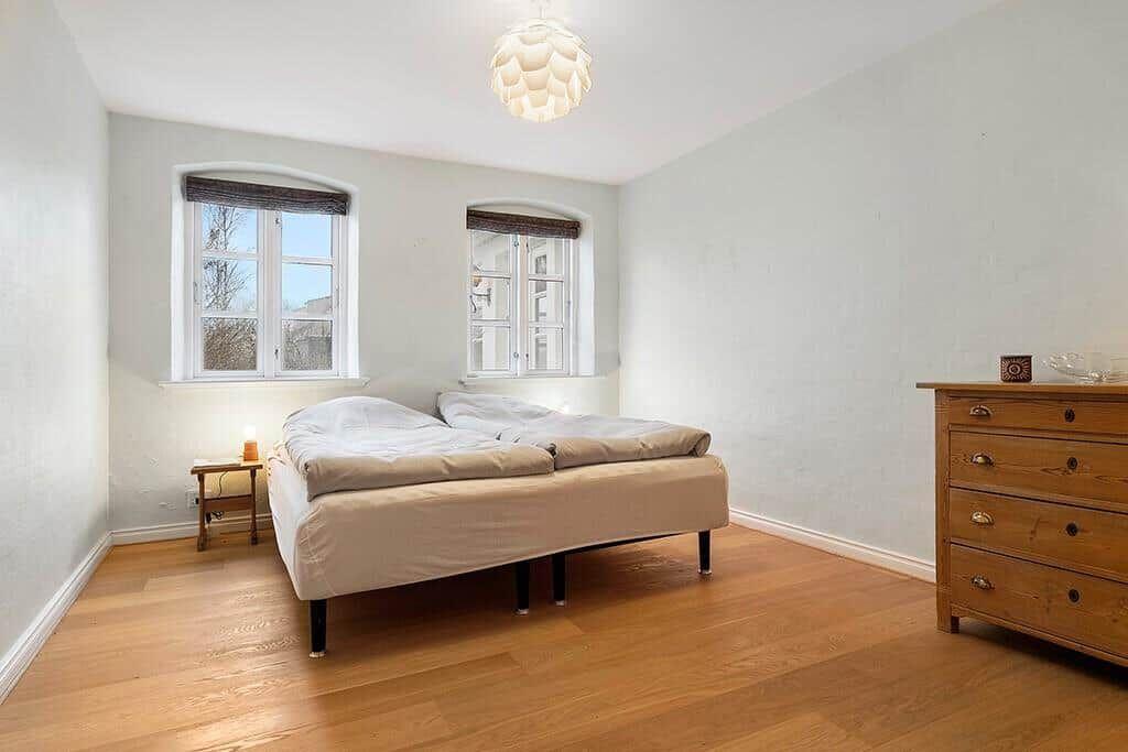 Bedroom with bed, two windows, and hardwood floor.
