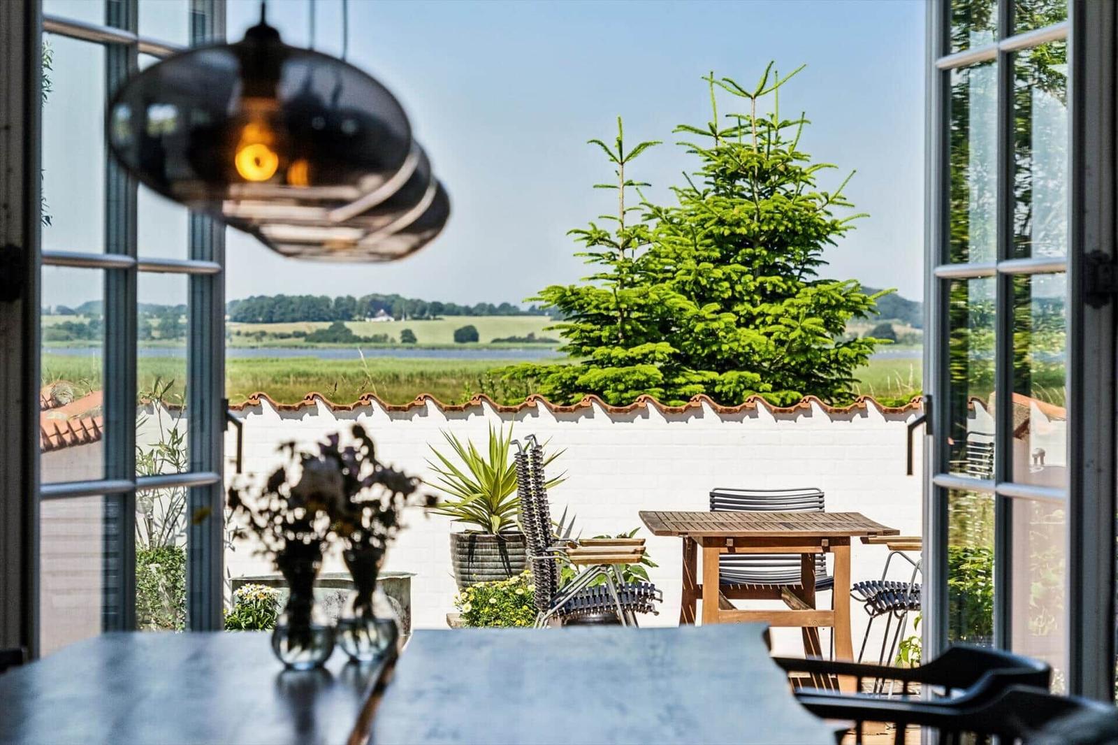 Terrace with table and chairs, view of green landscape and a lake.