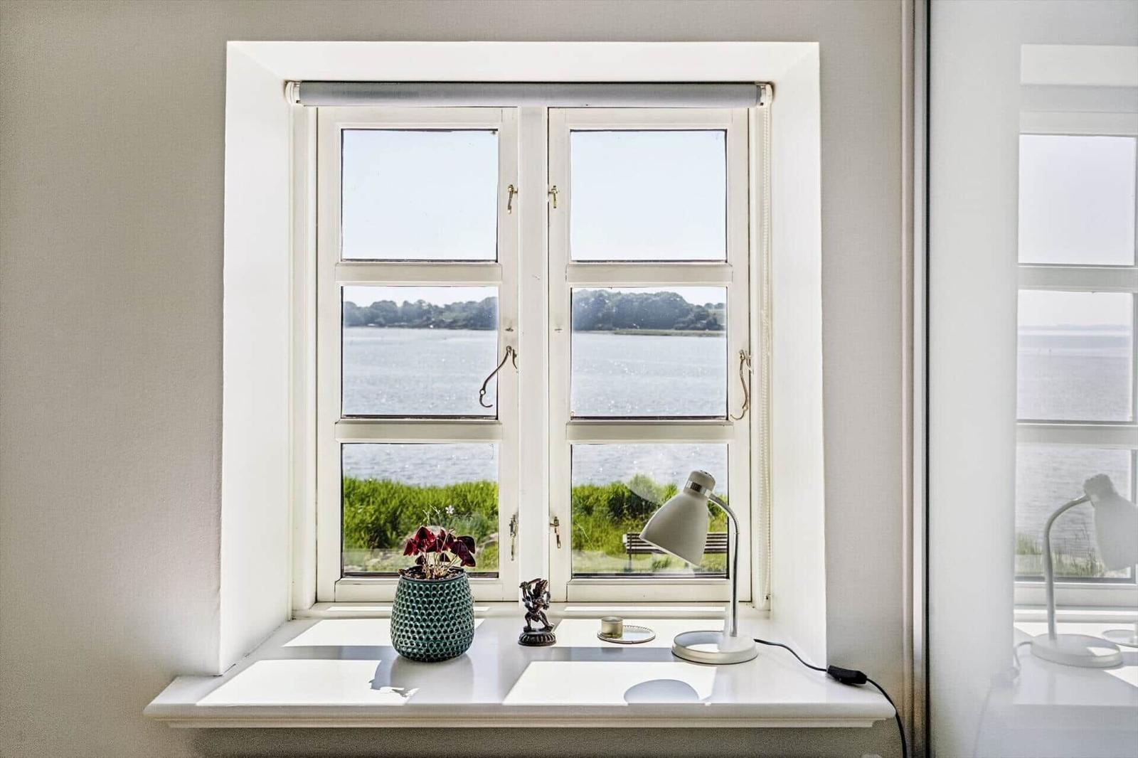 Window with view of water and greenery. On sill: plant, lamp, and decor.