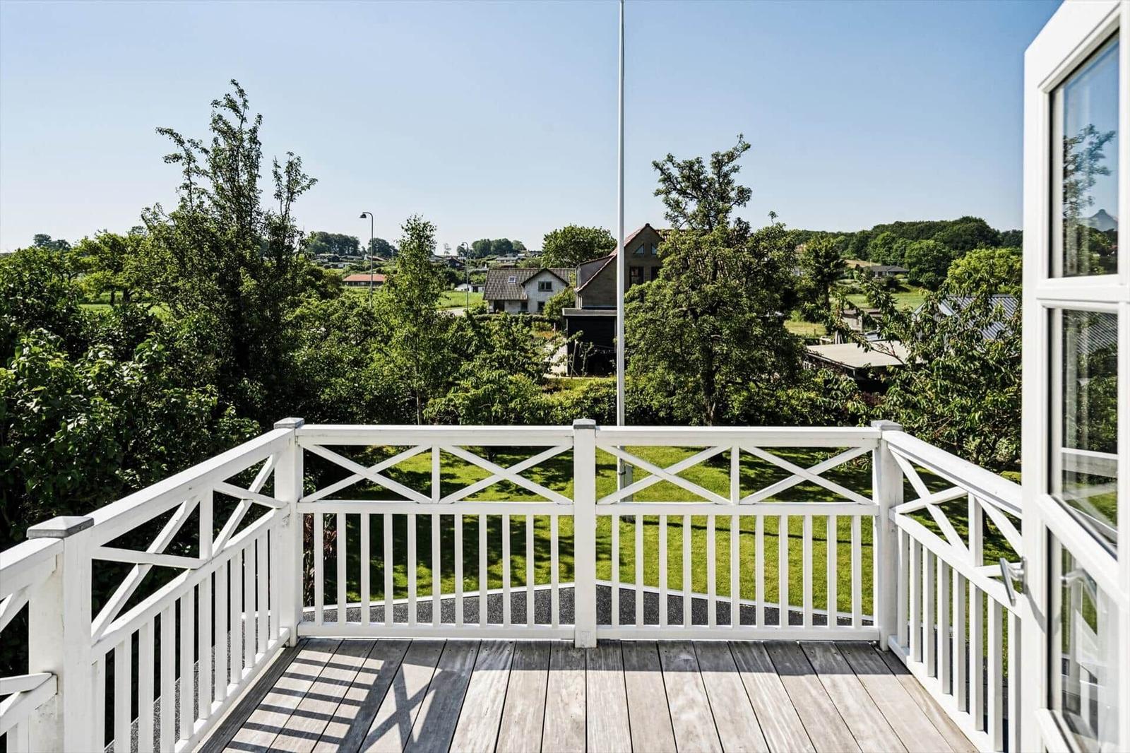 Deck with white railing and view of green landscape and houses.