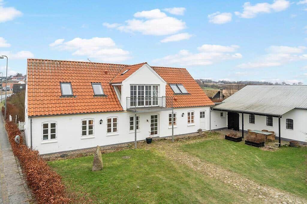 White house with red tiled roof and balcony. Lawn and outbuilding.