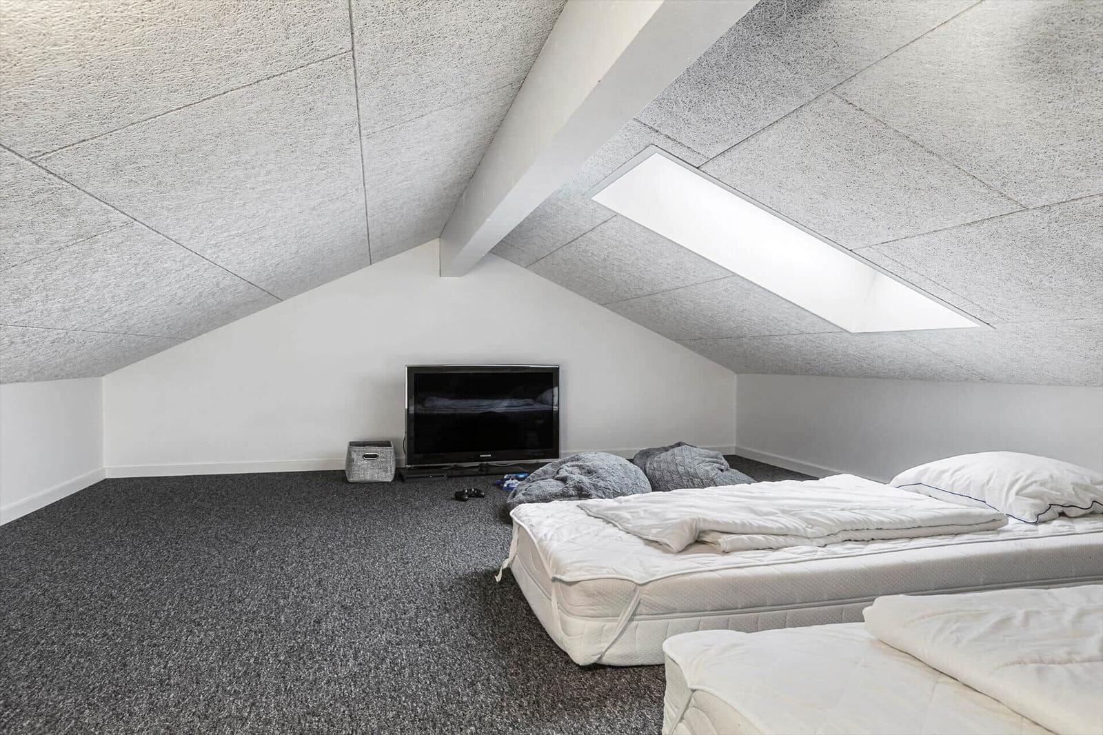 Room with sloped ceiling, mattresses, and TV
