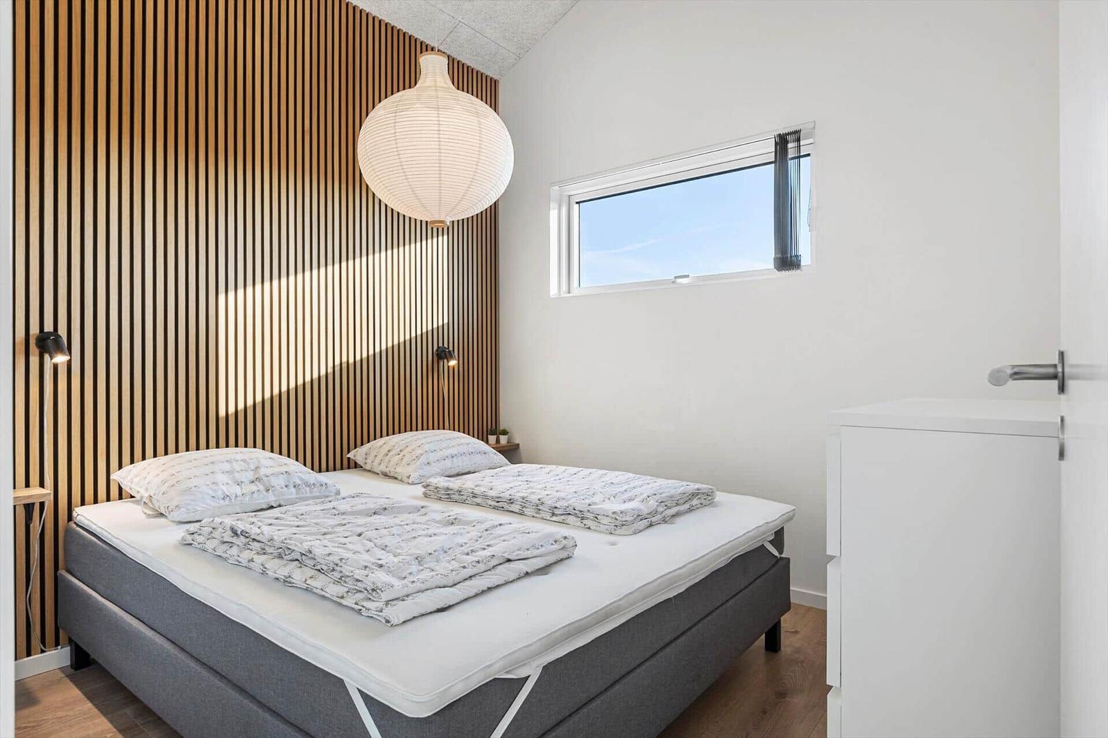 Bedroom with bed, wooden wall, window, and lamps.