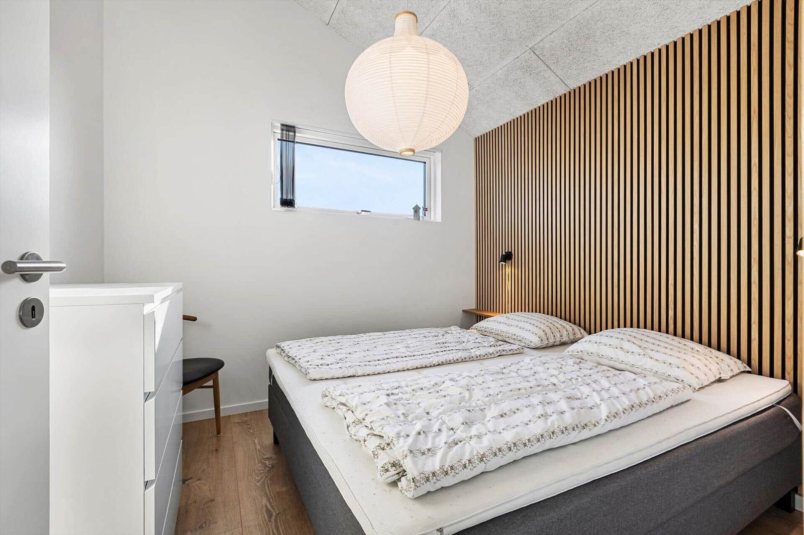 Bedroom with bed, wooden wall, and window.