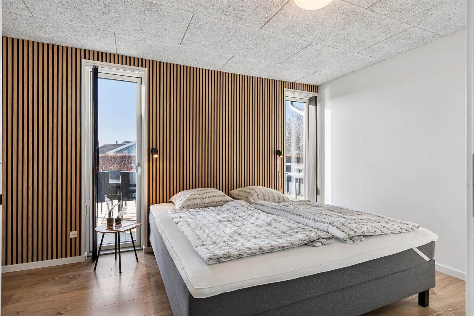 Bedroom with double bed, wooden wall, and balcony door.