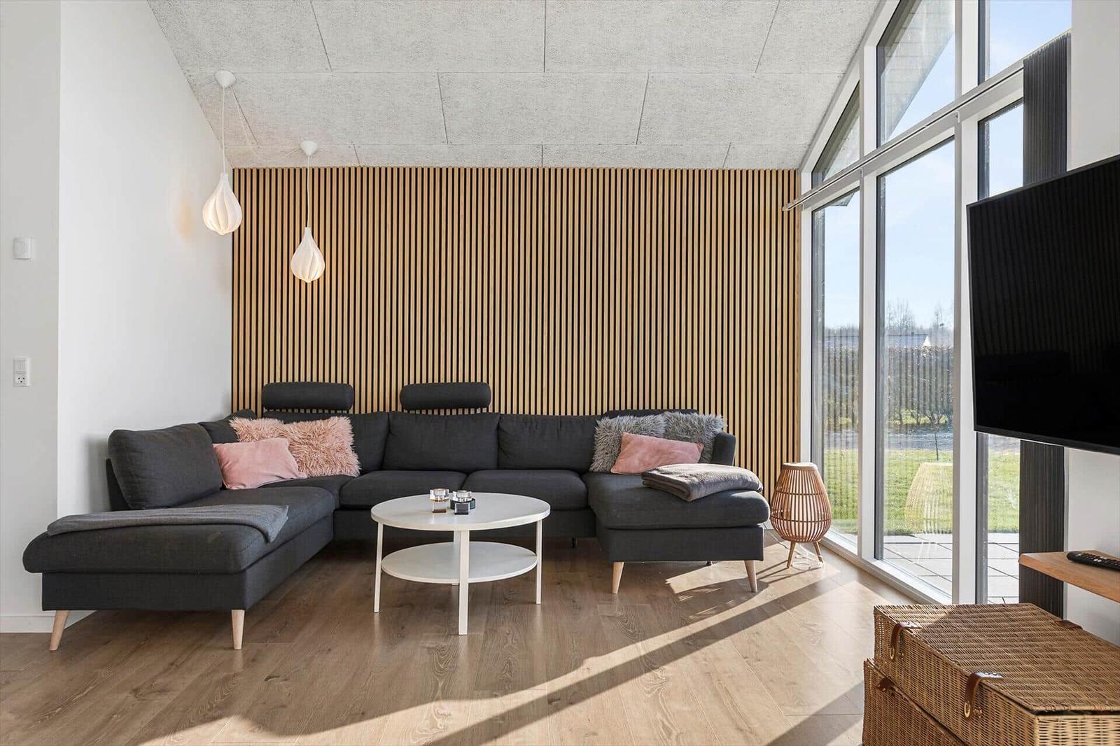 A living room with gray sofa, wooden wall, and large window.