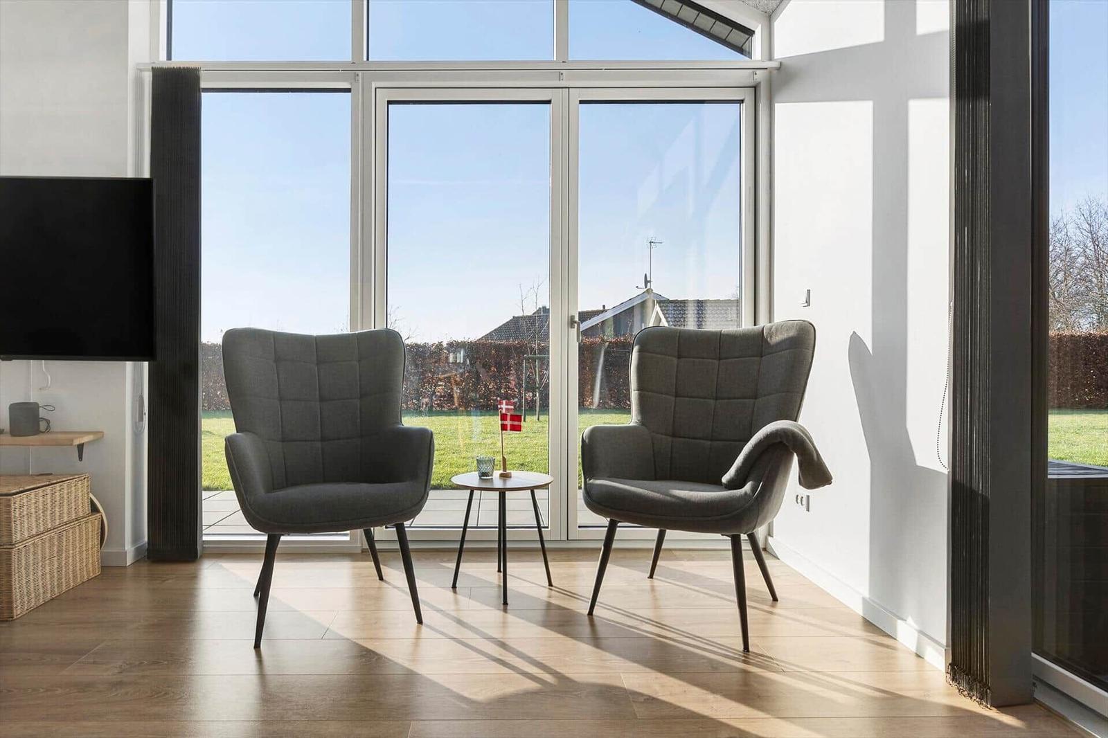 Two gray chairs sit before large windows overlooking a garden.