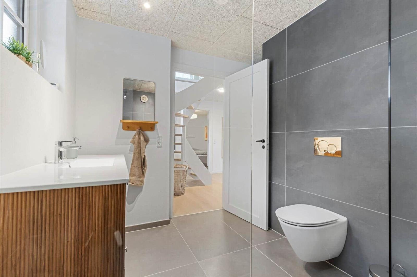 Badezimmer mit Waschbecken, Toilette und Dusche. Durchgang zur Treppe.