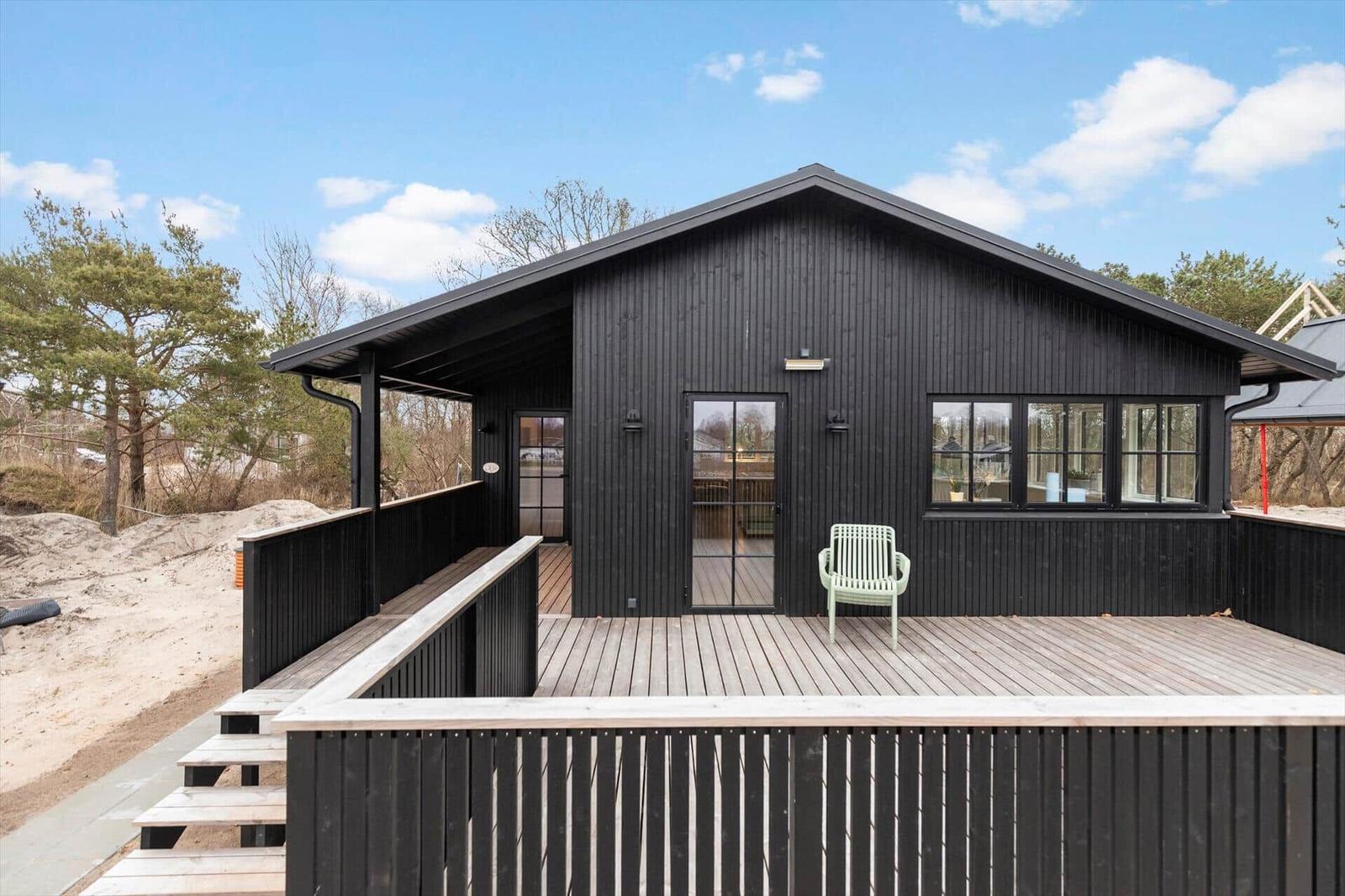 Schwarzes Holzhaus mit Terrasse und Stufen zur Strandnähe.