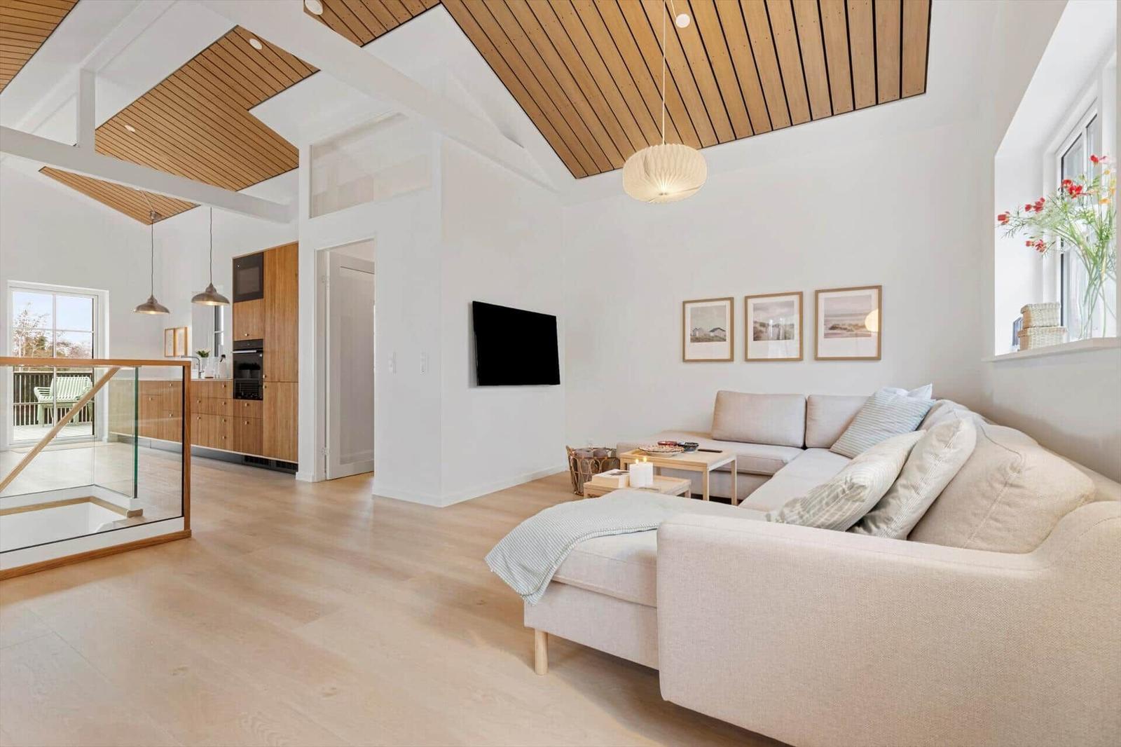 Wohnbereich mit Sofa, Fernseher und Holzdecke. Küche im Hintergrund sichtbar.