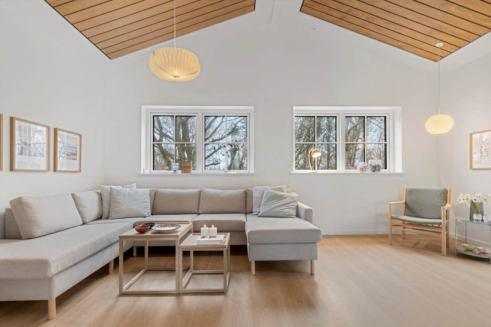 Wohnzimmer mit Sofa, Tischen und Fenstern. Holzdecke und helle Wände.