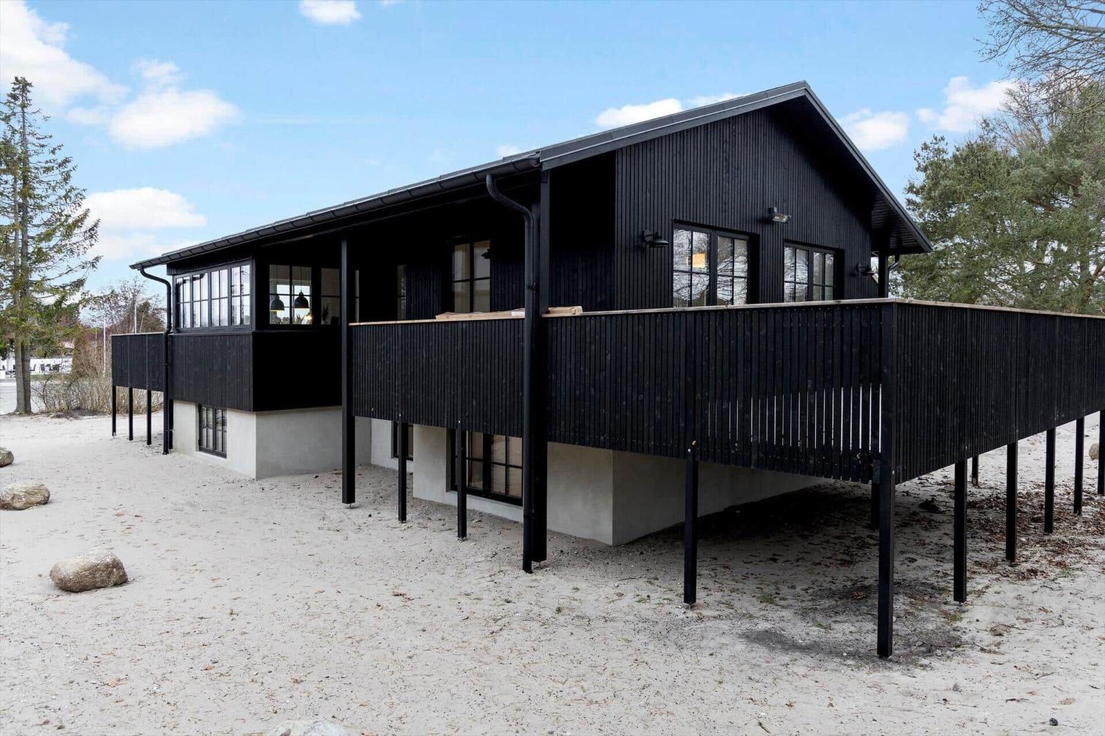 Schwarzes Haus mit Balkon auf Sandstrand, umgeben von Bäumen.