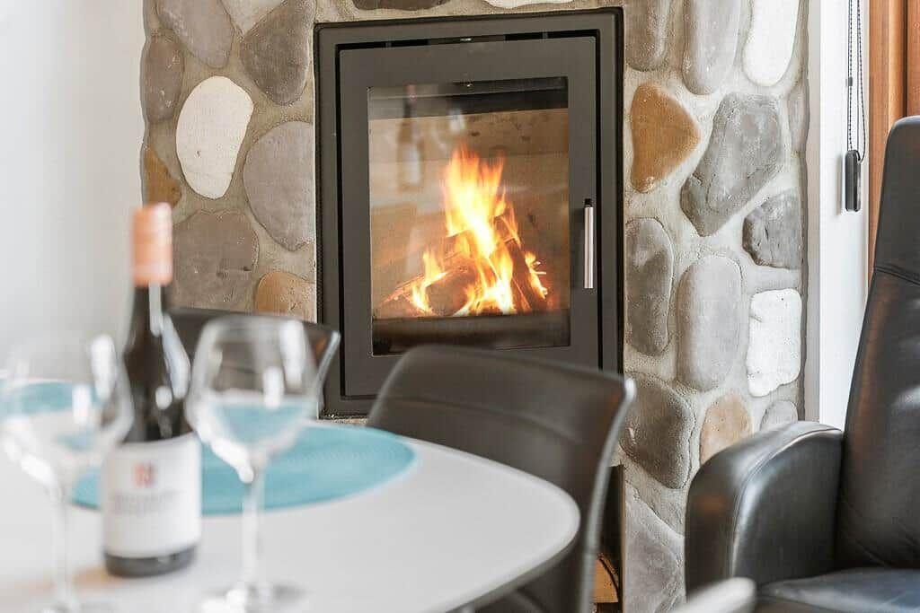 Feuer im Kamin, Tisch mit Weinglas und Flasche, schwarze Sessel